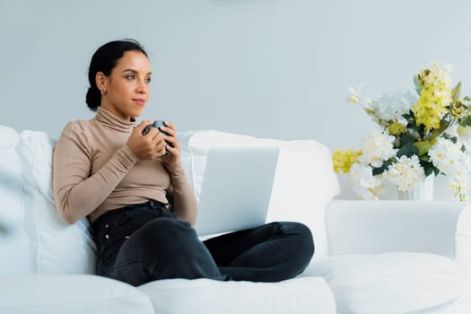 Happy woman drinking coffee on a sofa at home for crucial rest and relaxation. Portrait of young African American woman holding a cup.