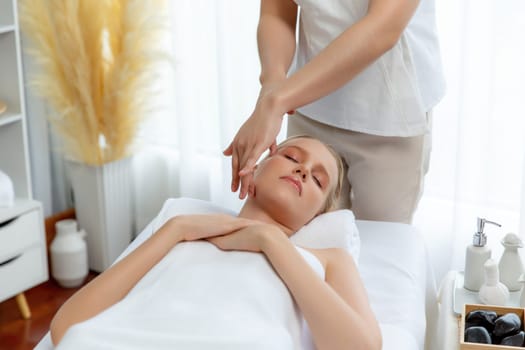 Caucasian woman enjoying relaxing anti-stress head massage and pampering facial beauty skin recreation leisure in dayspa modern light ambient at luxury resort or hotel spa salon. Quiescent