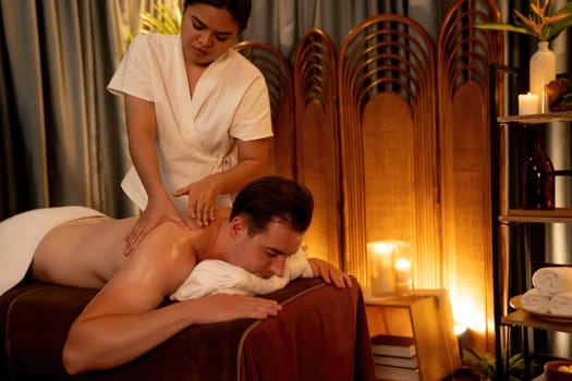 Caucasian man customer enjoying relaxing anti-stress spa massage and pampering with beauty skin recreation leisure in warm candle lighting ambient salon spa at luxury resort or hotel. Quiescent