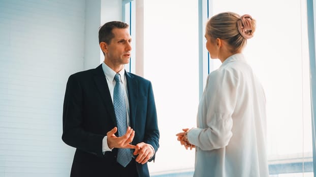 Two business people talk project strategy at office meeting room. Businessman discuss project planning with colleague at modern workplace while having conversation and advice on financial report. Jivy