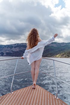 Woman on a yacht. Happy model in a swimsuit posing on a yacht against a blue sky with clouds and mountains.