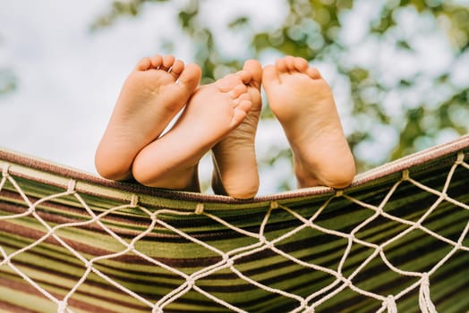Feet of children, which swinging on hammock at summer. Kids enjoying, boys dreaming resting together under tree. Happy childhood. High quality
