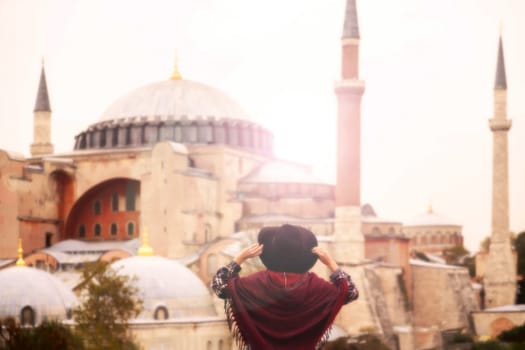 A young pretty girl in a stylish hat and a plaid shirt poses, makes a selfie on the phone next to the Hagia Sophia mosque. Tourism in Istanbul, Turkey.