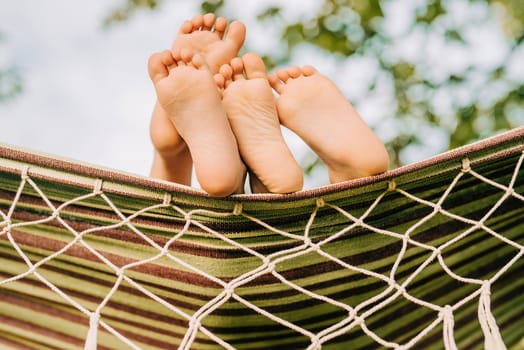 Feet of children, which swinging on hammock at summer. Kids enjoying, boys dreaming resting together under tree. Happy childhood. High quality