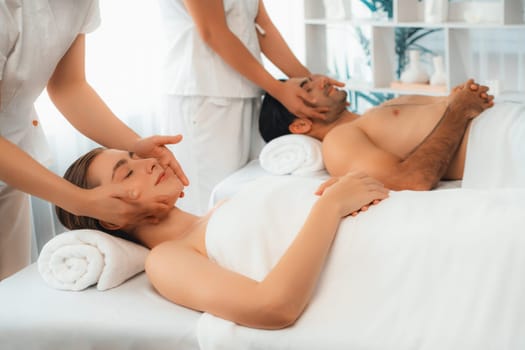 Caucasian couple enjoying relaxing anti-stress head massage and pampering facial beauty skin recreation leisure in dayspa modern light ambient at luxury resort or hotel spa salon. Quiescent