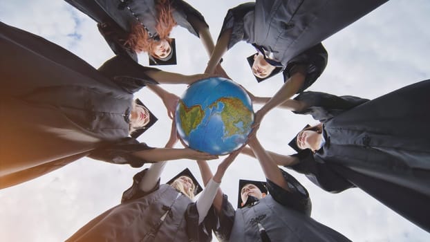 Graduating students hug and toss a geographical globe of the world overlooking north and south america. The concept of preserving peace.