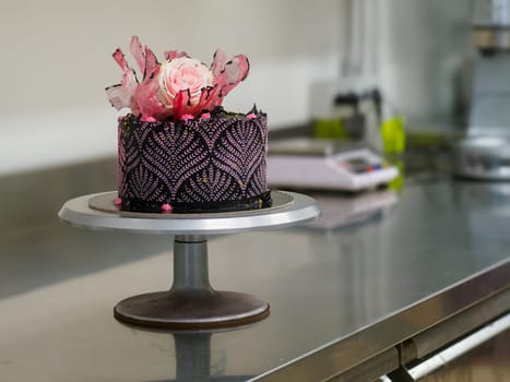 frosted icing black decorate cake for birthday celebration, real rose topping and pink sweet swirls in professional kitchen