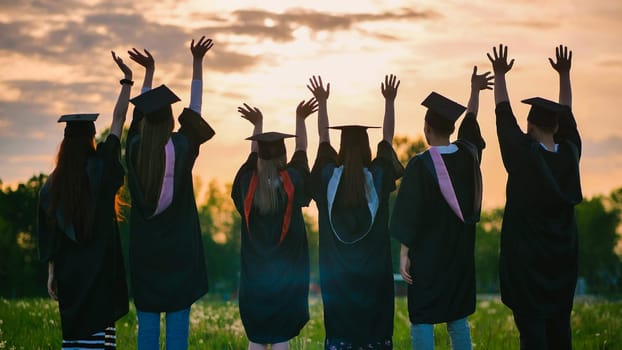 Silhouettes of graduates in suits at sunset waving to the sun