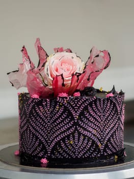 frosted icing black decorate cake for birthday celebration, real rose topping and pink sweet swirls in professional kitchen