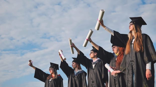 Cheerful graduates pose with raised diplomas on a sunny day