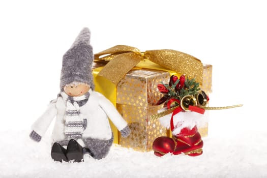 Little doll sitting next to Christmas present and red Santa boot in the snow against white background