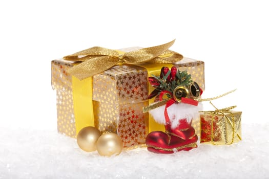 Package with bow,golden balls and a red Santa boot lying in the snow against a white background