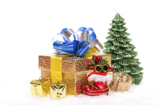 Package with bow,red Santa boot,golden walnut and a candle Christmas tree standing in the snow against white background