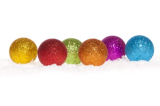 Colorful shiny Christmas tree baubles lying in the snow against white background