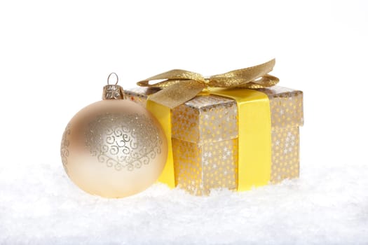 Package with bow and big golden balls lying in the snow against white background