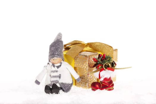 Little doll sitting next to Christmas present and red Santa boot in the snow against white background