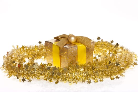Package with bow and golden ball lying in the snow against white background