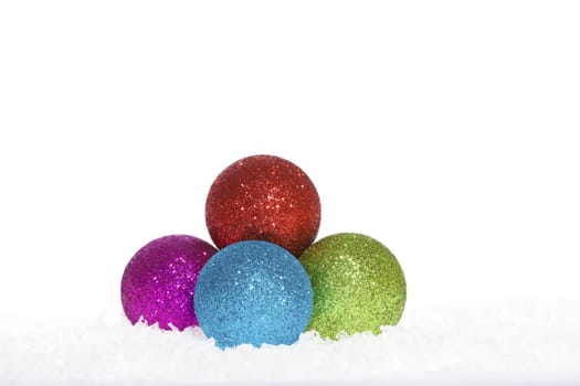 Colorful shiny Christmas tree baubles lying in the snow against white background