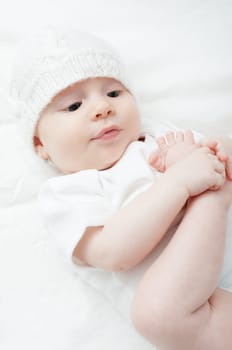 Cute Baby in Knitted Cap Girl Playing With Her Toes on White Background