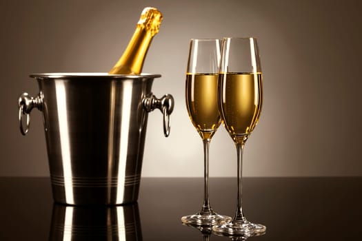 Two glasses of champagne with a bottle of sparkling wine in a cooler on black mirror