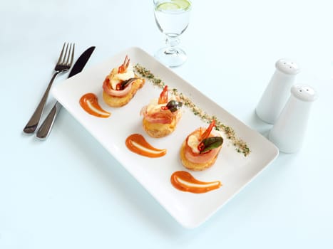 Delicious and delicate shrimps wrapped in bacon on potato slices with a spinach leaf.