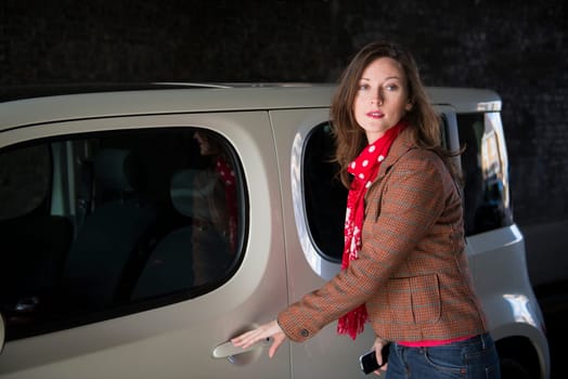 Beautiful fashionable young woman looking around before opening her car