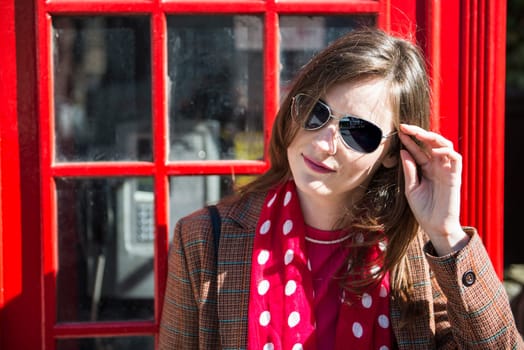 Portrait of beautiful young woman wearing sun glasses and leaning against London red phone booth