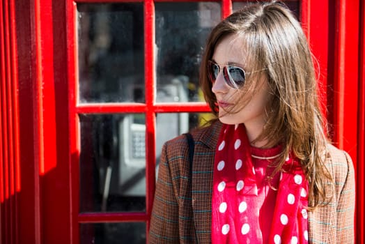 Portrait of beautiful young woman wearing sun glasses and leaning against London red phone booth