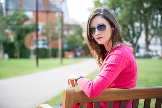 Portrait of beautiful young woman sitting on bench in park