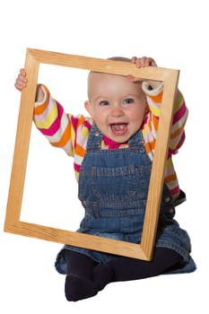 Laughing vivacious little baby girl playing with an empty wooden picture frame looking through it at the camera