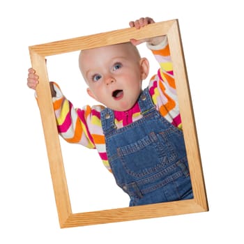 Little baby girl holding up an empty wooden picture frame around her face with a look of amazement isolated on white