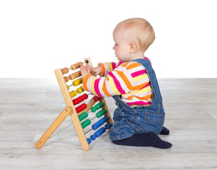Cute little baby girl kneeling on the floor in dungarees playing with a colourful abacus moving the counters as she learns