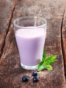 Glass of delicious creamy blueberry yoghurt smoothie with mint on rustic textured wooden boards