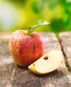 Quartered apple showing juicy the juicy flesh together with a whole fruit on an old textured wooden table outdoors