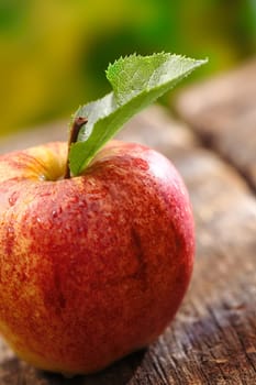 Closeup of a ripe red apple with a single leaf on an old wooden table with shallow depth of field