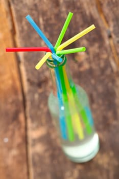 Arrangement of colourful drinking straws radiating from the neck of a glass bottle containing a fruit drink with shallow dof
