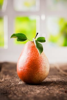 Tasty ripe red and yellow pear with leaves on a rough wooden table indoors with window background