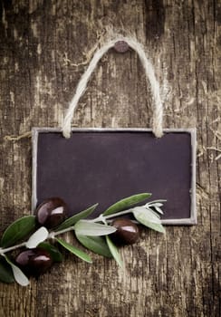Fresh black olives lying with a slate blackboard on an old grungy weathered and textured wooden table