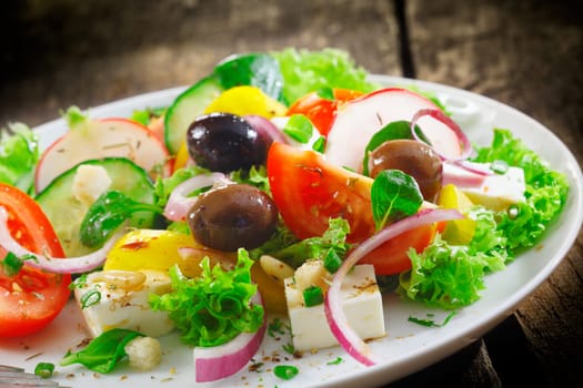 Closeup view of a plate of fresh healthy Greek salad with lettuce, basil, feta, onion, olives, radish and tomato