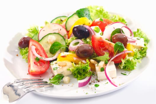 Healthy Greek salad served for lunch with crisp leafy greens, olives, feta, onion , tomato, cucumber and radish on a white background
