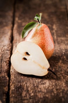 Halved fresh juicy pear balanced against a whole fruit on a rough wooden table top