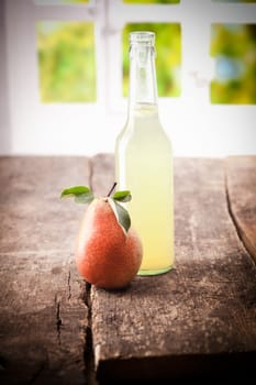 Ripe fresh red pear standing on an old wooden table with a glass bottle of pure squeezed juice