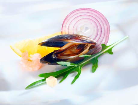 Single open marine mussel with rocket and lemon and a slice of red onion on a white background