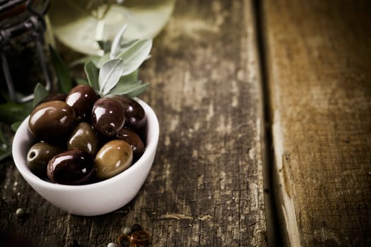 Bowl of fresh whole black olives with copyspace on a grungy old textured wooden tabletop