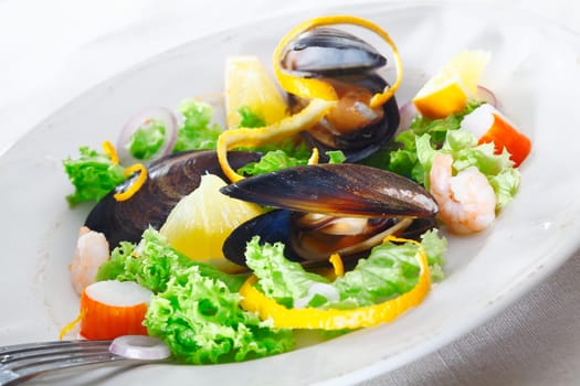 Serving of delicious seafood salad with mussels, crab and shrimp on a bed of crisp green lettuce garnished with orange peel