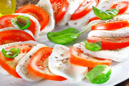 Artistically arranged cheese and tomato salad in alternating slices of red and white garnished with fresh herbs