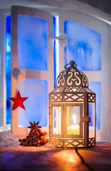 Christmas lantern with a glowing candle burning in a window illuminating dried seasonal spices with copyspace