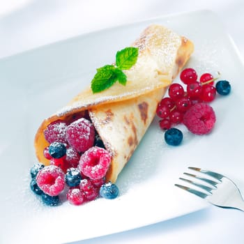 Berry pancake sprinkled with sugar with an assortment or ripe raspberries, redcurrant and blueberries garnished with mint