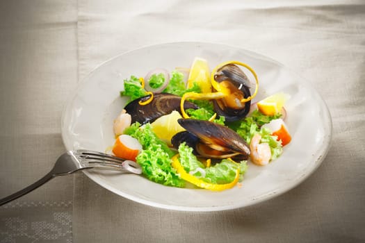 Serving on a plate of fresh mussel and seafood salad with leafy greens, crab and prawns garnished with orange peel