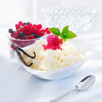Tasty creamy rice dessert served with raspberries and redcurrants and garnished with mint and vanilla pods